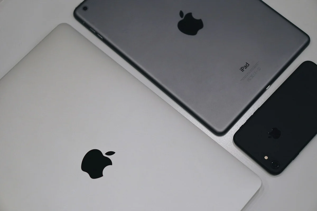 A gray iPhone, iPad, and MacBook side by side on a white table