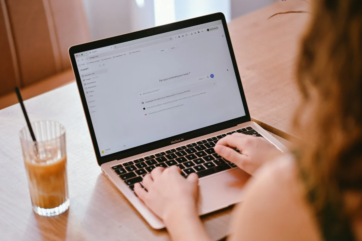 A person typing on a laptop next to a glass of iced coffee