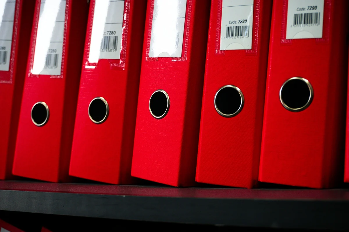 A row of red file binders lined up on a storage shelf