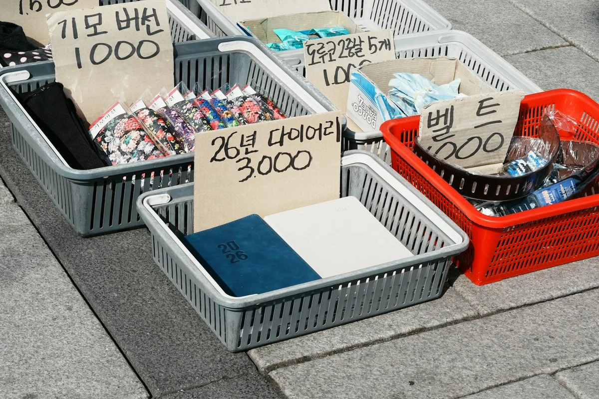 Baskets of goods on a sidewalk, each with a cardboard sign showing the product name and price in large letters