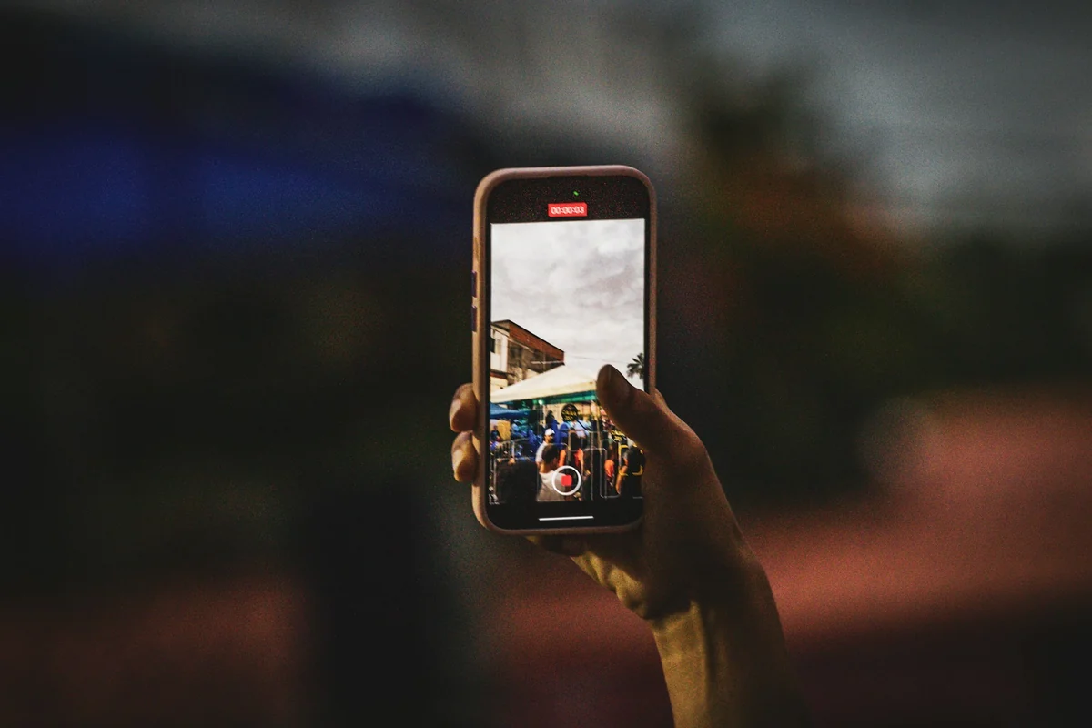 A hand holds a phone recording a vertical video, with the record button on screen