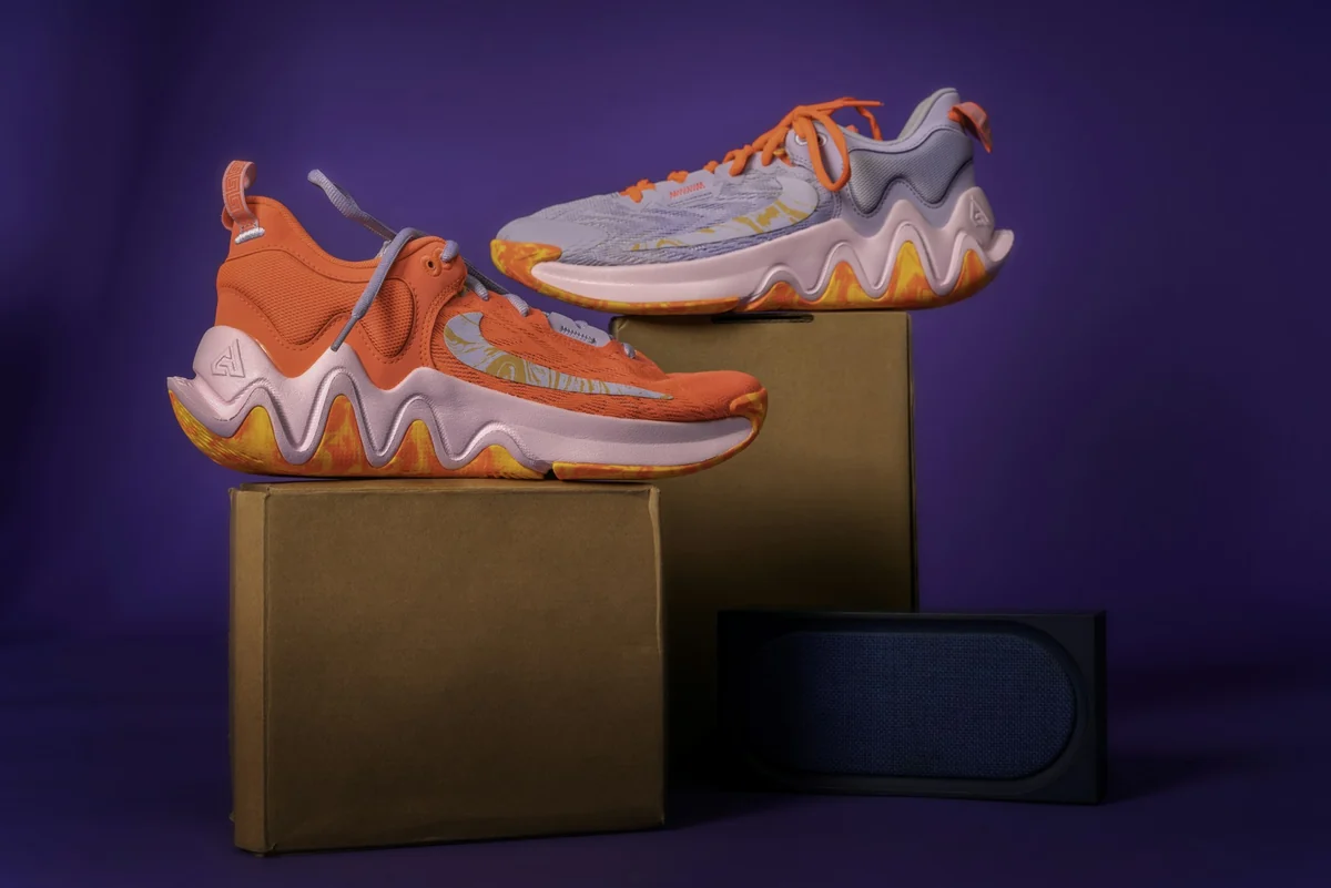A pair of orange and purple sneakers placed on two cardboard boxes against a deep purple background