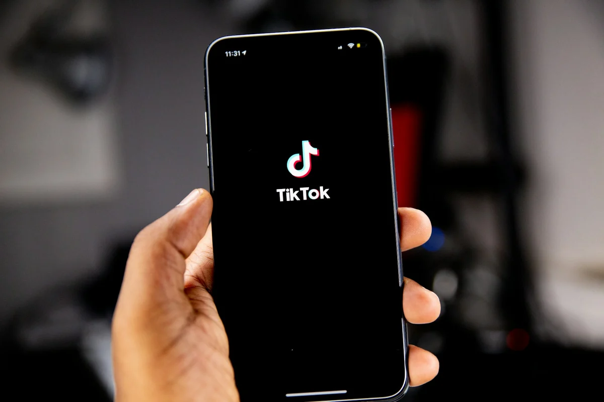 A hand holding a phone upright, with the TikTok logo on the screen