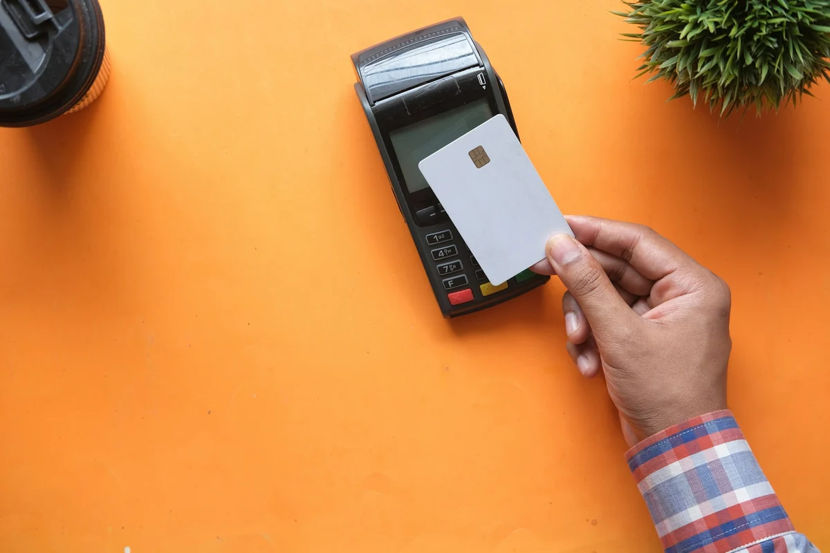 A hand holding a payment card against a card reader on an orange table