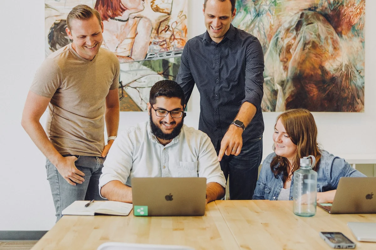 Four smiling coworkers looking at a laptop screen together at a meeting table