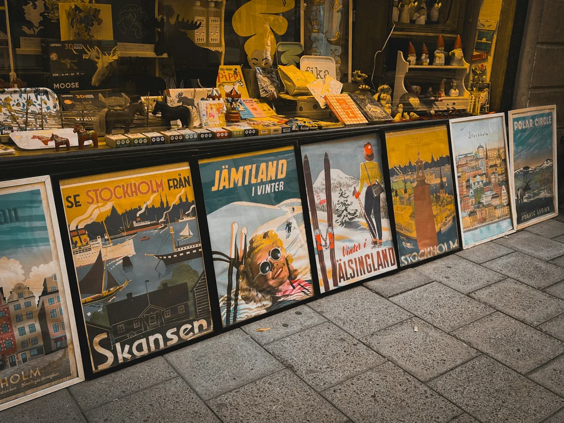 A row of vintage-style travel posters in front of a shop, each with a large headline and an illustration