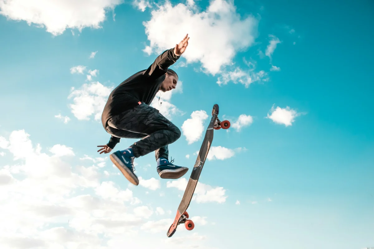 A skateboarder jumps against a blue, cloudy sky with the board spinning beside him