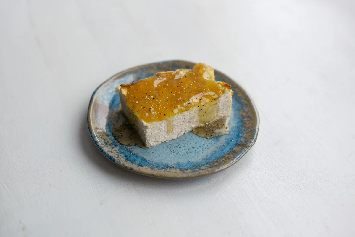 A slice of cake with a slightly runny orange glaze on a blue glazed ceramic plate