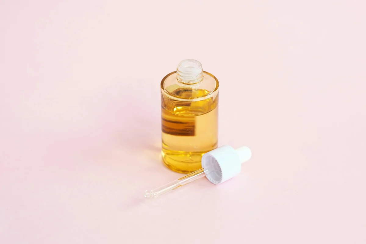 A serum bottle and dropper placed to one side on a plain pale pink background, with most of the frame left empty