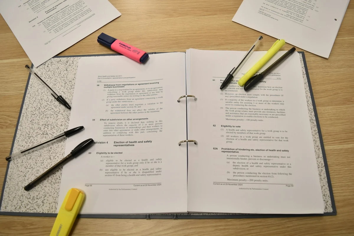 An open document on a wooden desk with pink and yellow highlighters and a pen for marking key points
