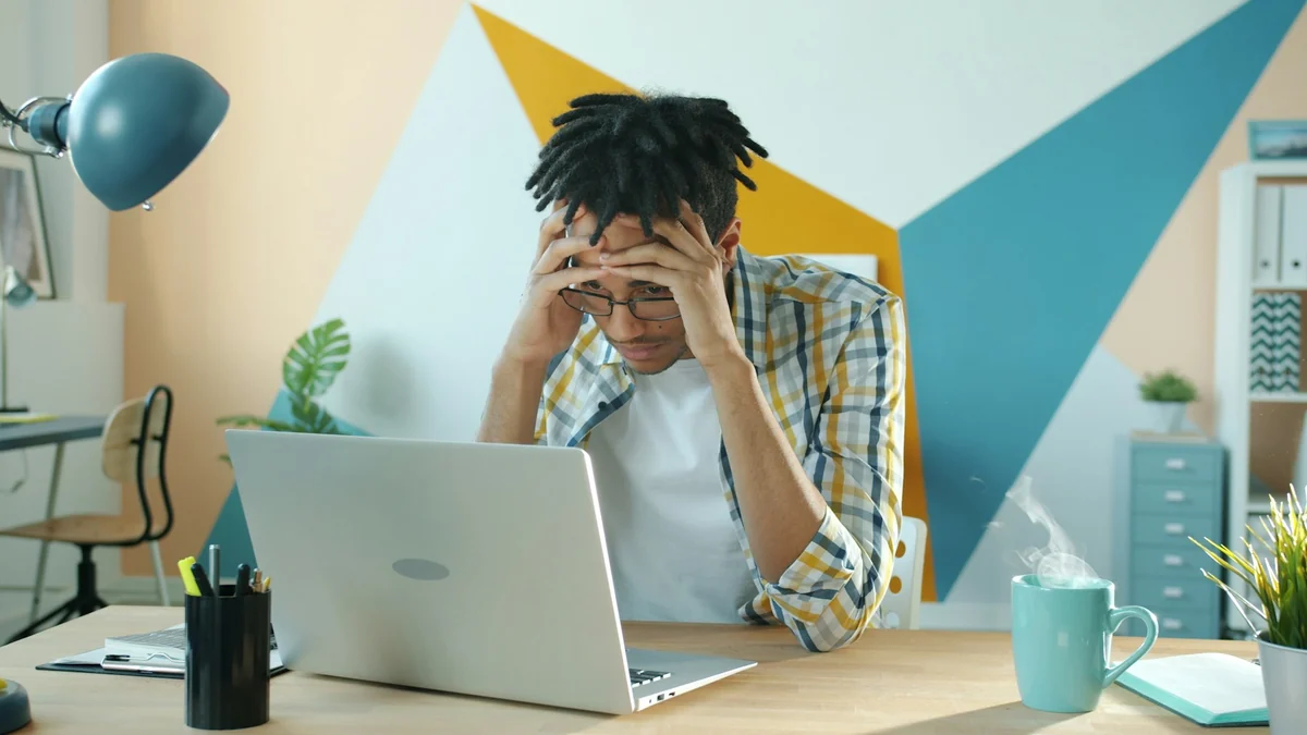A person holding their head in front of a laptop because the video result did not turn out as planned