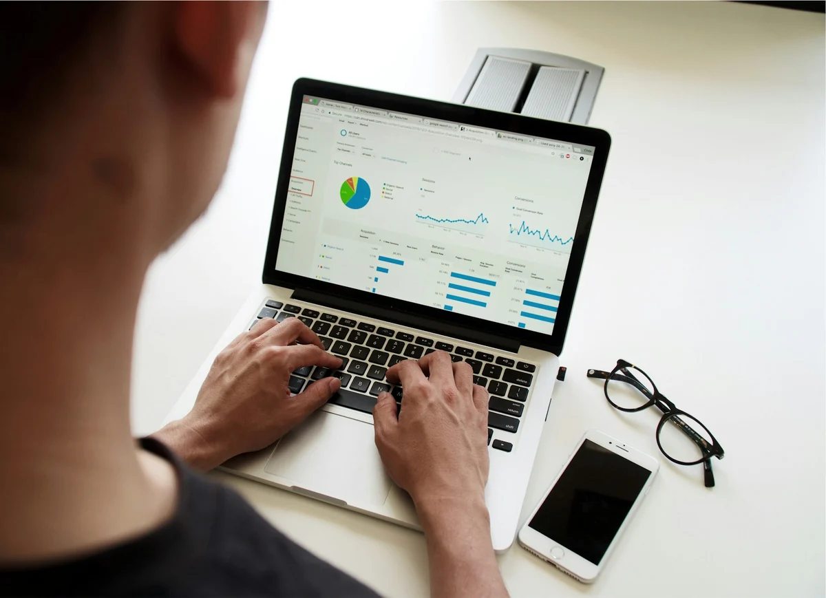 A person typing on a laptop and looking at a campaign data dashboard, next to a phone and a pair of glasses
