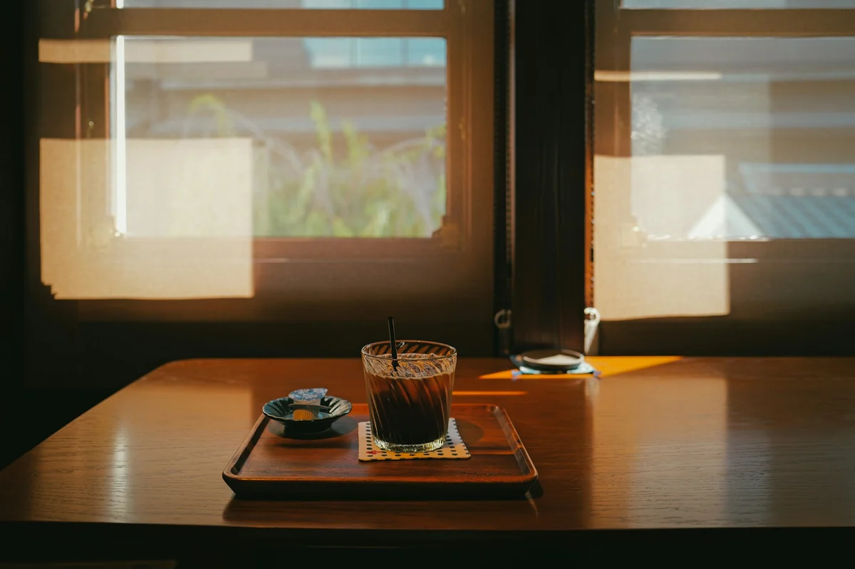 An iced coffee on a wooden tray by a window, with sunlight slanting across the table