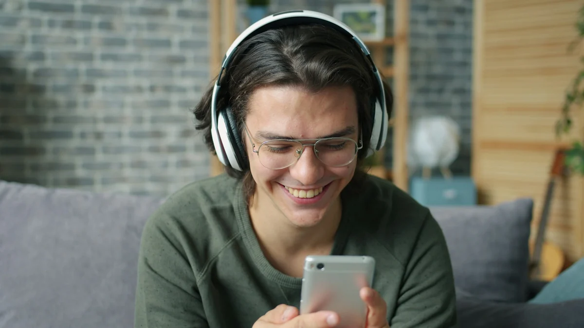 A young man in over-ear headphones smiles while watching a video on his phone