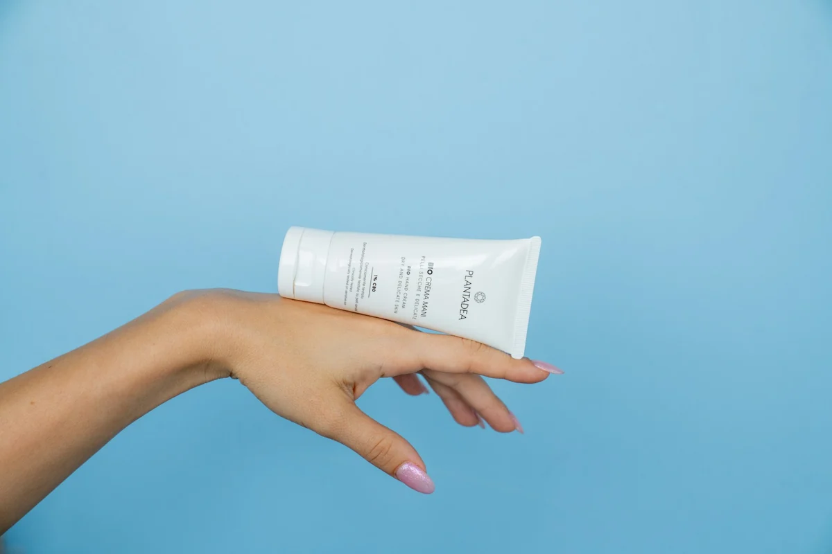 A hand placing a white tube of moisturizer on a green background, the product filling the frame