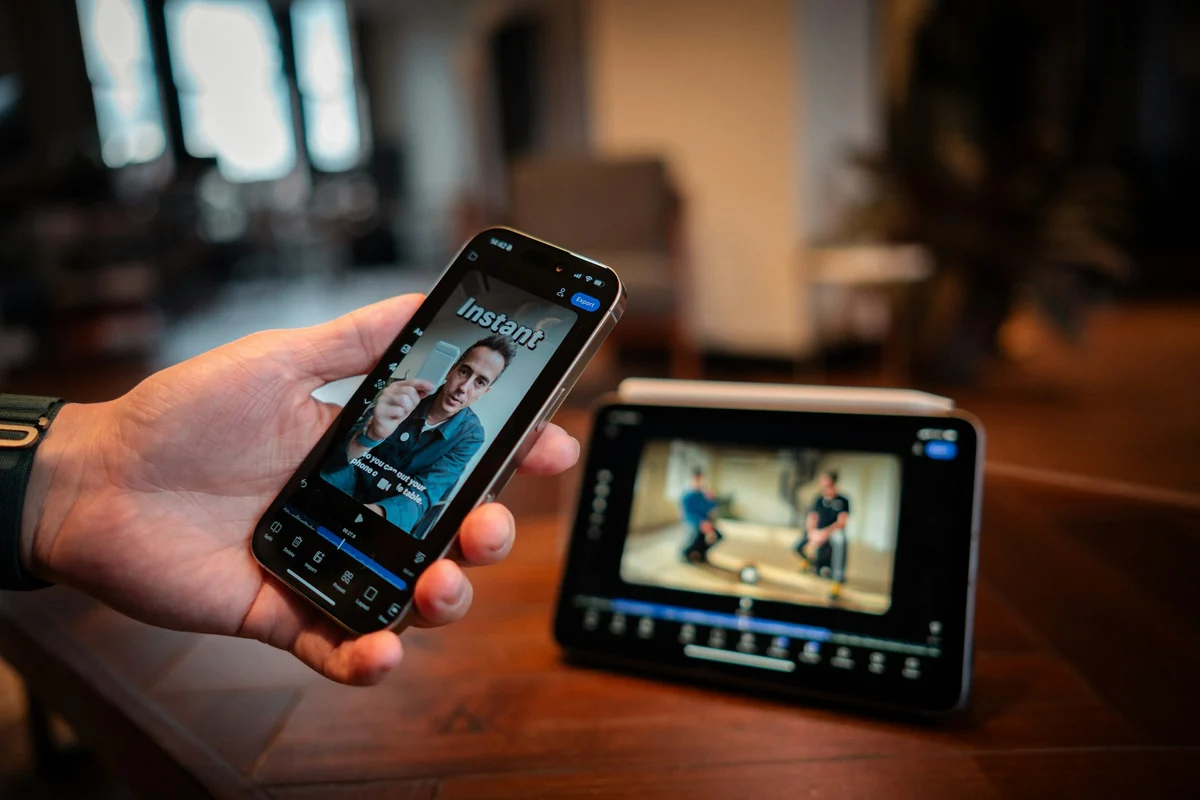 A hand holding a phone that is editing a video with large text and captions over the image, a tablet behind it