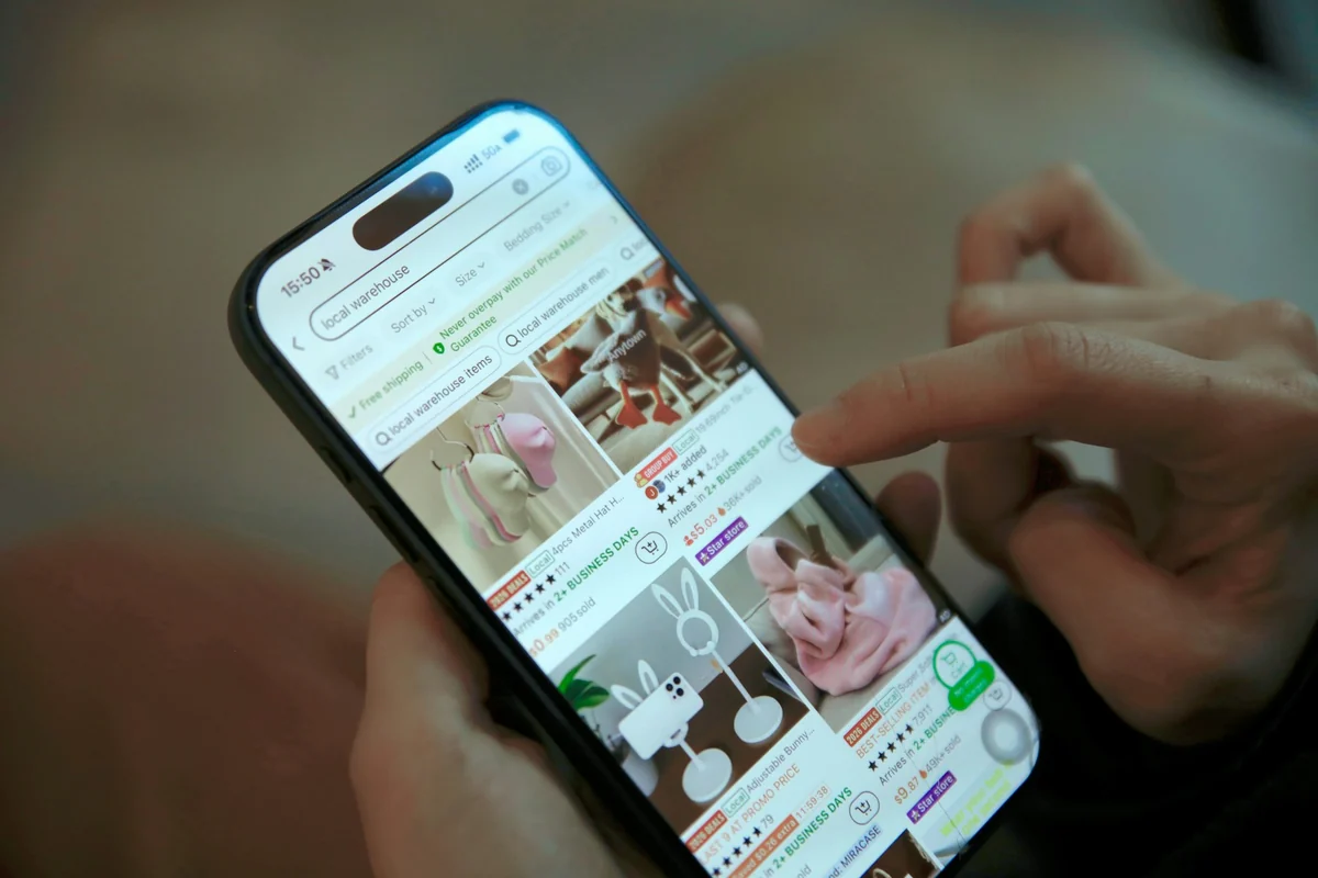 A hand scrolling a shopping app on a phone with a grid of product photos