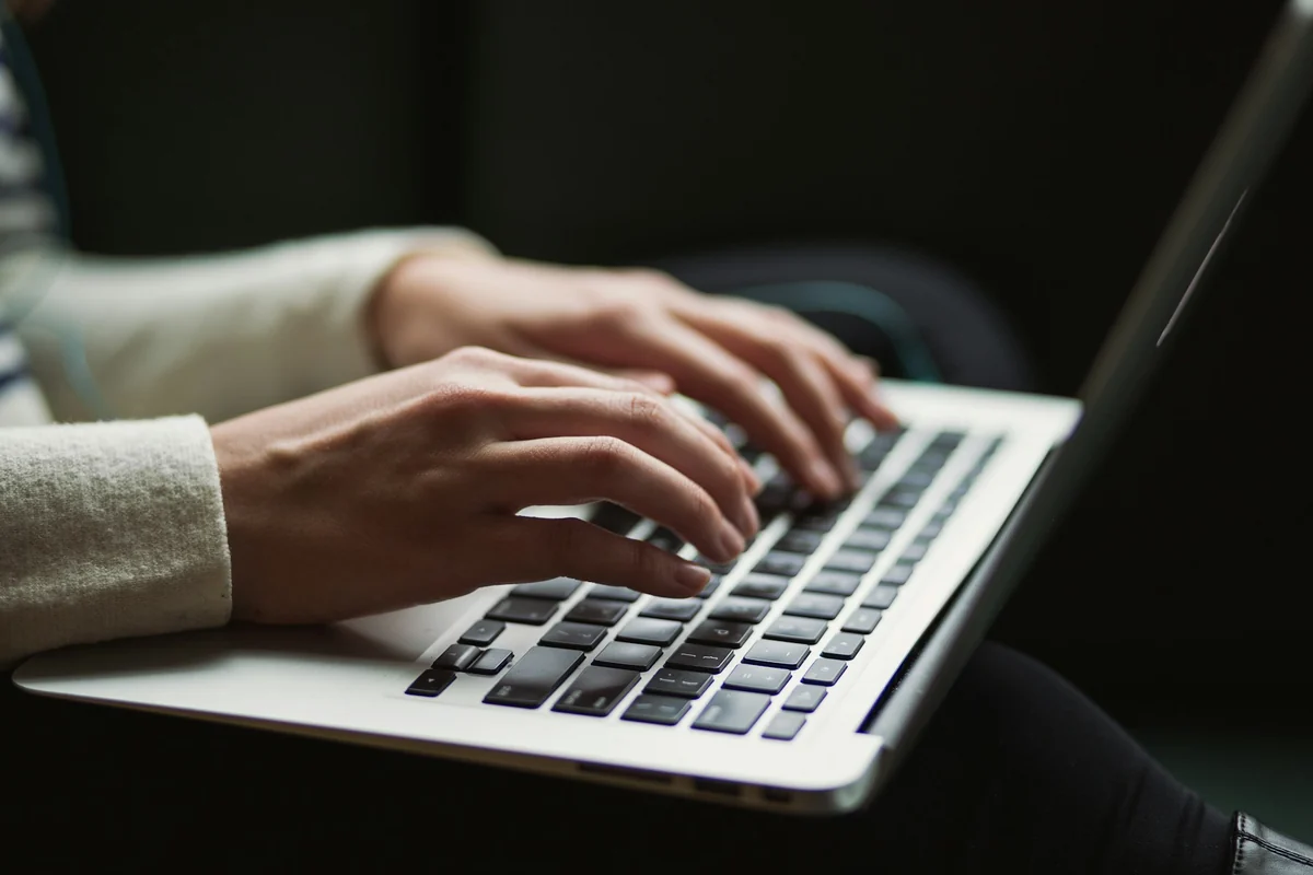 Two hands with a ring and a watch typing on a laptop keyboard on a wooden desk