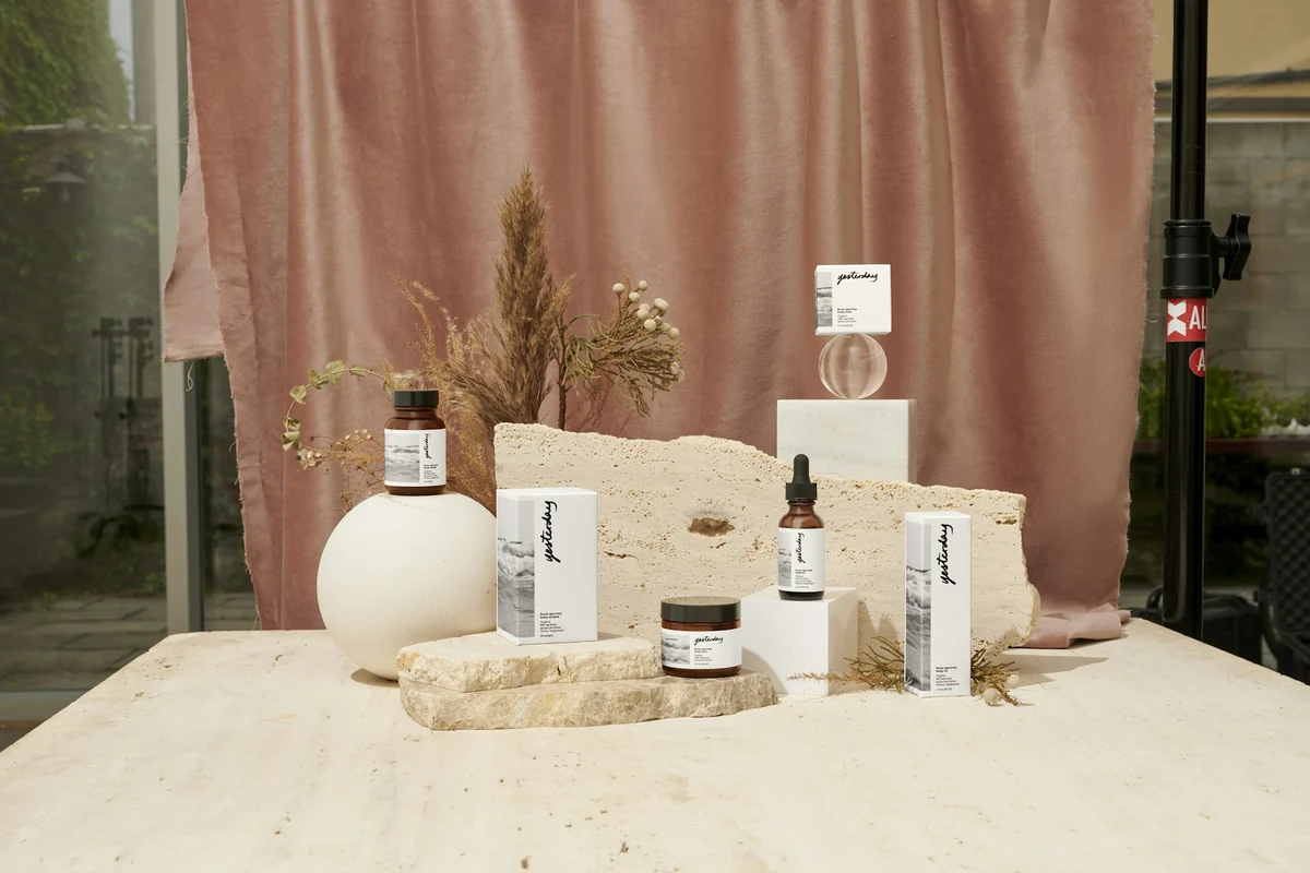 Bottles and cosmetic boxes stacked on rocks in front of a pink curtain during a product photo shoot