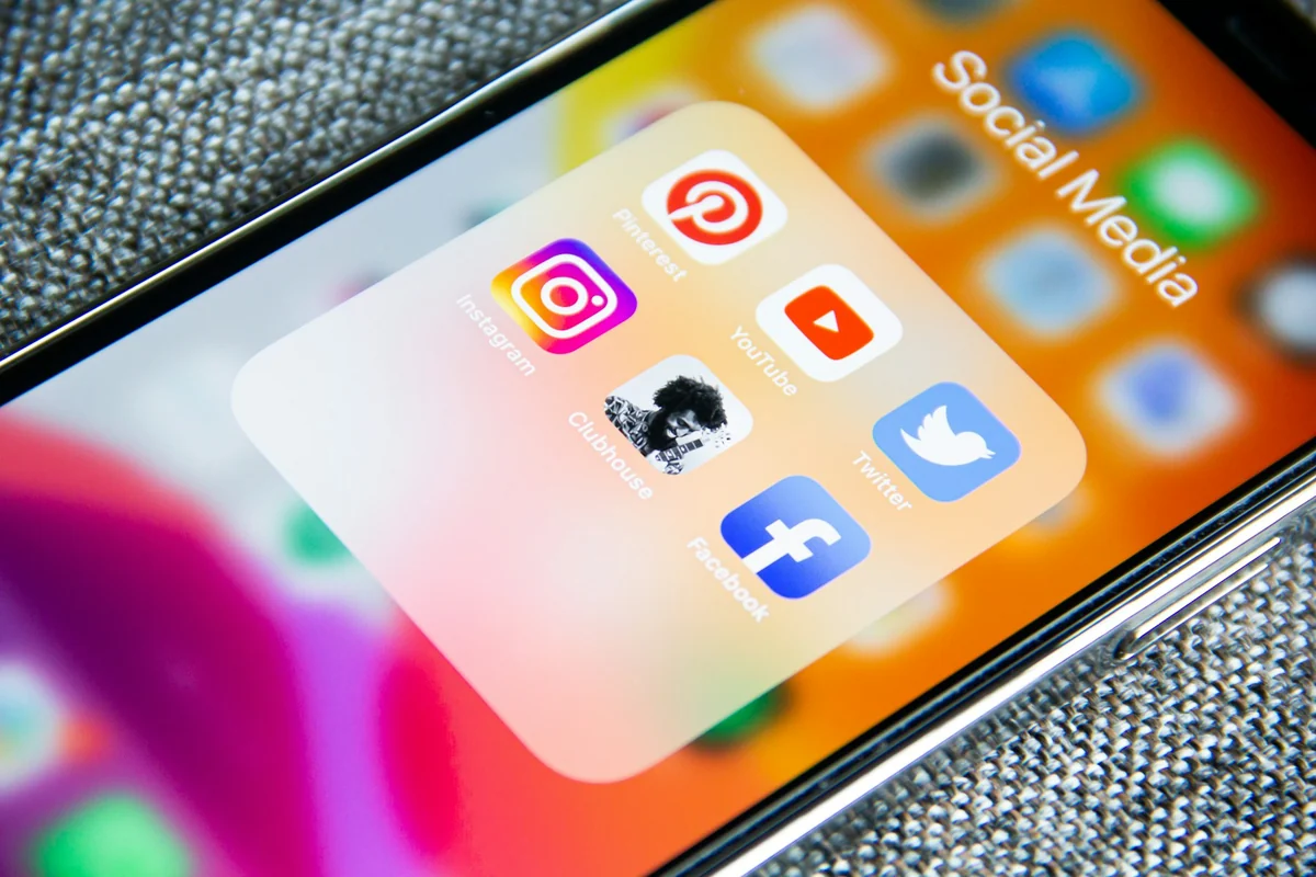 A hand holding a phone with a folder of social media apps open on the home screen