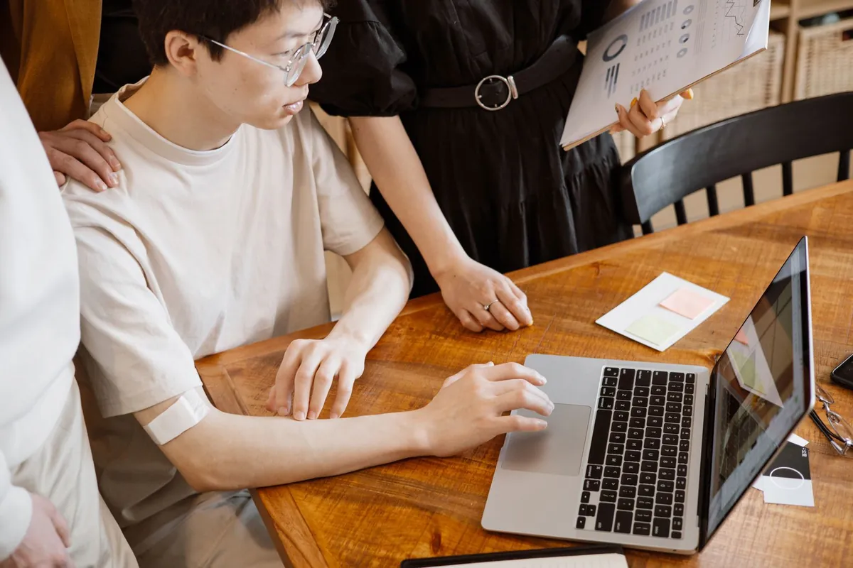 An employee checking ad numbers on a laptop while a manager stands beside him asking how things are going