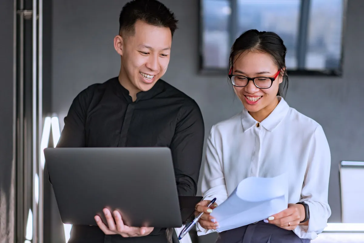 Two colleagues smiling while they read a report on a laptop